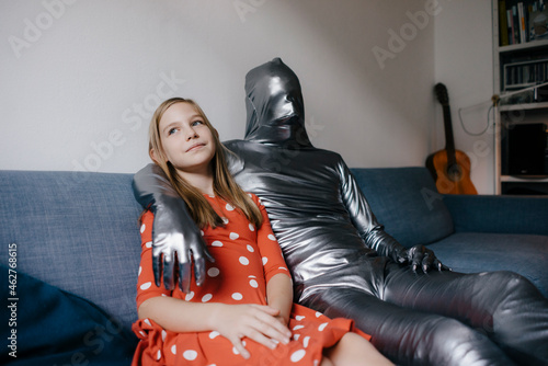 Man in morphsuit and girl sitting on couch at home photo