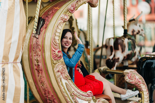 Happy pregnant woman waving while sitting on carousel at amusement park, Cascais, Portugal photo