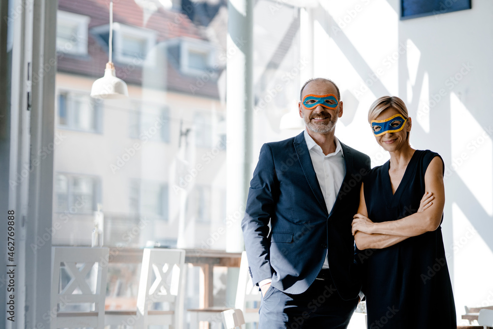Businessman and woman wearing super hero masks, standing in coffee shop