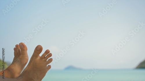 Bare feet of young man removing sand from foot lying on beach near calm azure ocean at exotic resort extreme closeup. Traveling to tropical countries