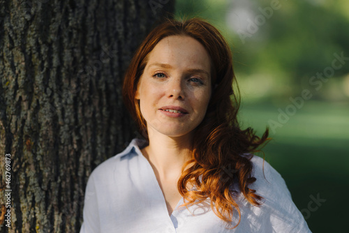 Portrait of redheaded woman at tree in a park