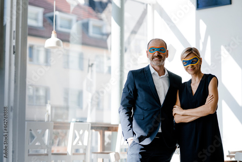 Businessman and woman wearing super hero masks, standing in coffee shop photo