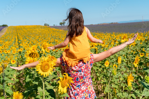 Mother carrying daughter on shoulders in sunflower field during summer photo