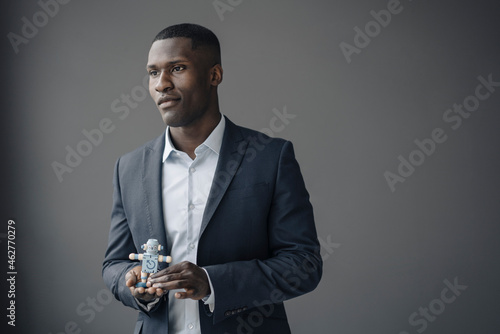 Portrait of young businessman with toy robot against grey background photo