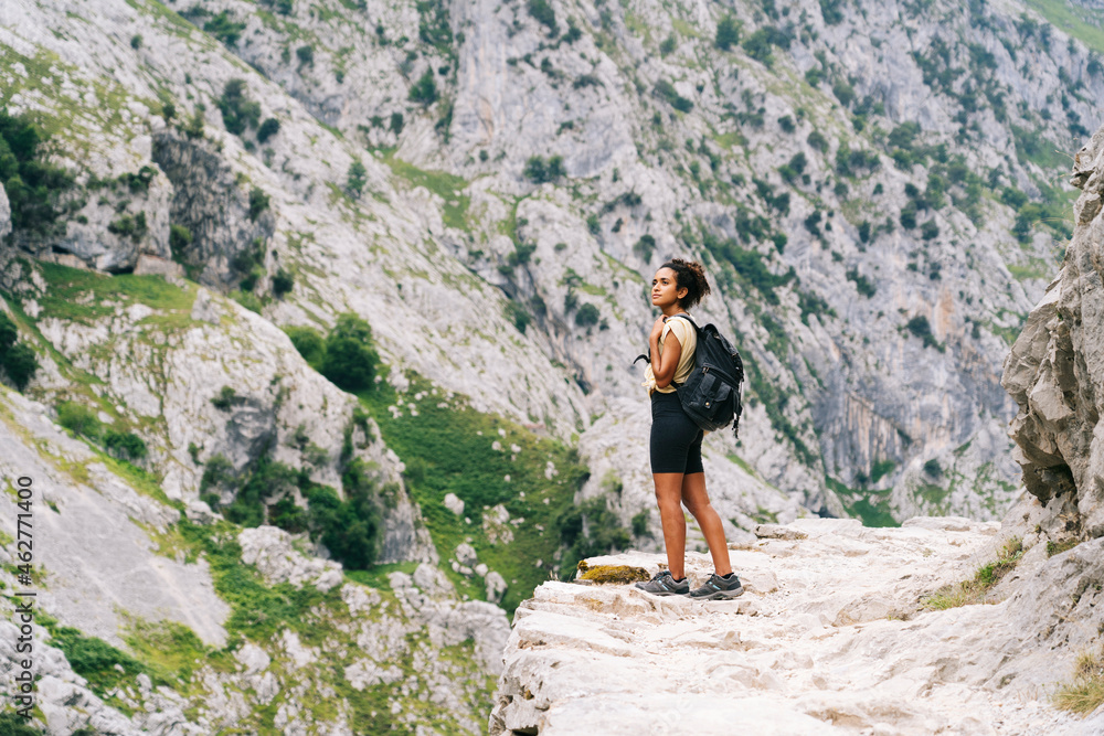 Woman with backpack admiring view while standing on mountain path at Ruta Del Cares, Asturias, Spain Woman with backpack admiring view while standing on mountain path at Ruta Del Cares, Asturias, Spain
