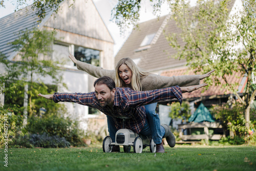 Laughing couple, pretending to fly on a toy car in the garden