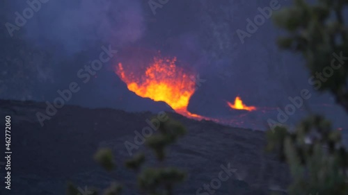 RACK FOCUS OF HALEMAUMAU SPEWING HOT LAVA WITH OHIA TREE IN FOREGROUND photo