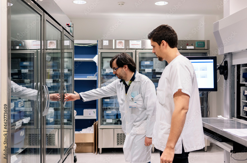 Doctor standing with male coworker opening refrigerator in pharmacy Doctor standing with male coworker opening refrigerator in pharmacy