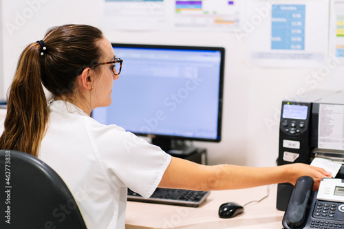 Female pharmacist using fax machine on desk while sitting in hospital photo