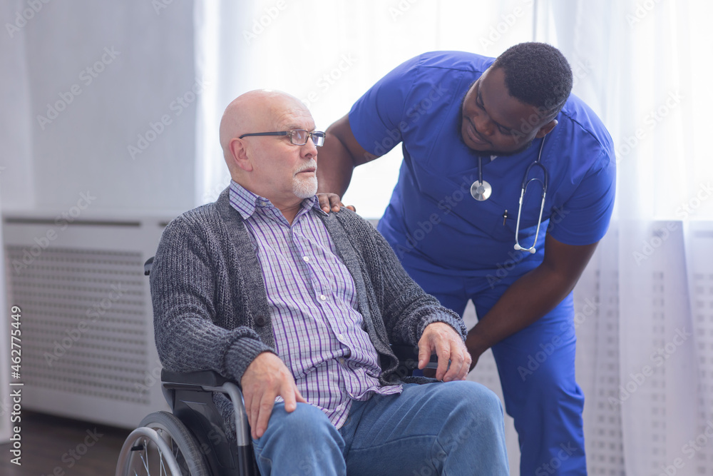 African-American caregiver and old disabled man in a wheelchair. Professional nurse and handicapped patient in a nursing home. Assistance, rehabilitation and health care. African-American caregiver and old disabled man in a wheelchair. Professional nurse and handicapped patient in a nursing home. Assistance, rehabilitation and health care.