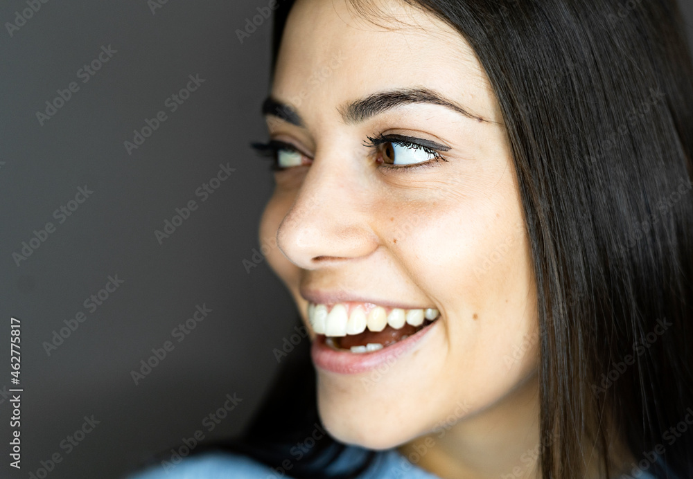 Close-up of smiling woman looking away while standing against gray background Close-up of smiling woman looking away while standing against gray background