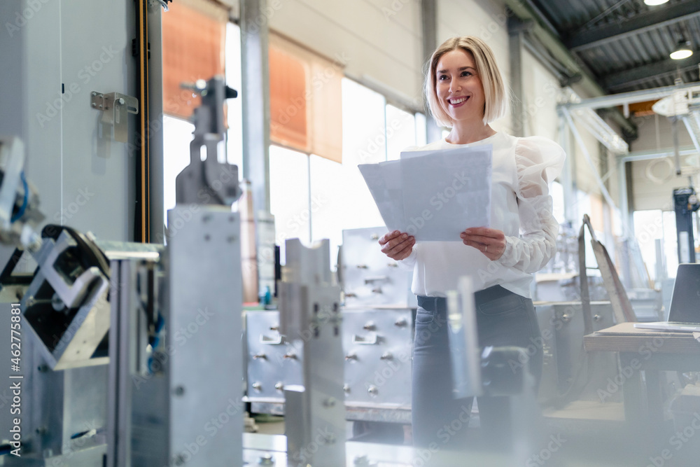 Portrait of a smiling young woman holding papers in a factory Portrait of a smiling young woman holding papers in a factory