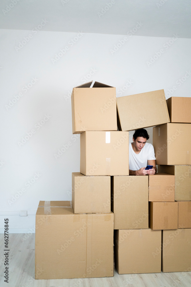 © Westend61 - Young man using smart phone while leaning on boxes in new house