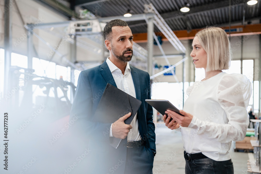 Businessman and young woman with tablet talking in a factory Businessman and young woman with tablet talking in a factory