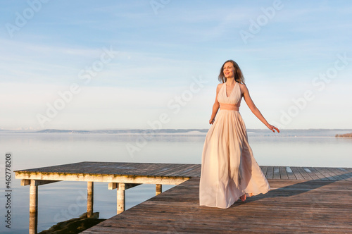 Full length of smiling beautiful woman walking on pier over lake against sky photo