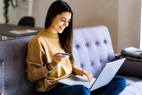 Young woman with credit card shopping over laptop while sitting at home