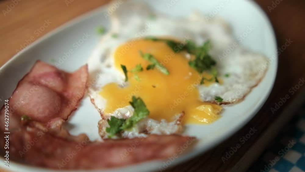 Delicious fried egg and bacon stripes with chopped herbs on white plate Delicious fried egg and bacon stripes with chopped herbs on white plate