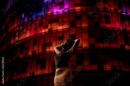 Woman with arms raised standing against red illuminated building in city photo