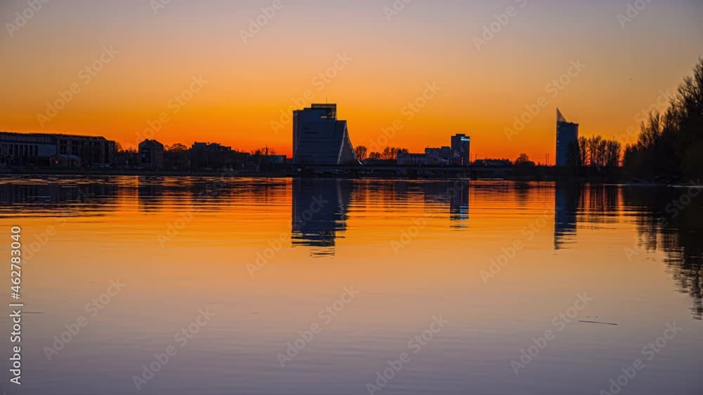 Time lapse shot of tranquil lake during golden sunset and silhouette of National Library of Latvia in background - Riga,Europe Time lapse shot of tranquil lake during golden sunset and silhouette of National Library of Latvia in background - Riga,Europe