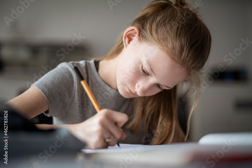 Girl learning at home, writing in exercise book