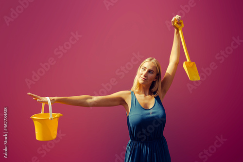 Young woman with sand bucket and shovel against purple photo