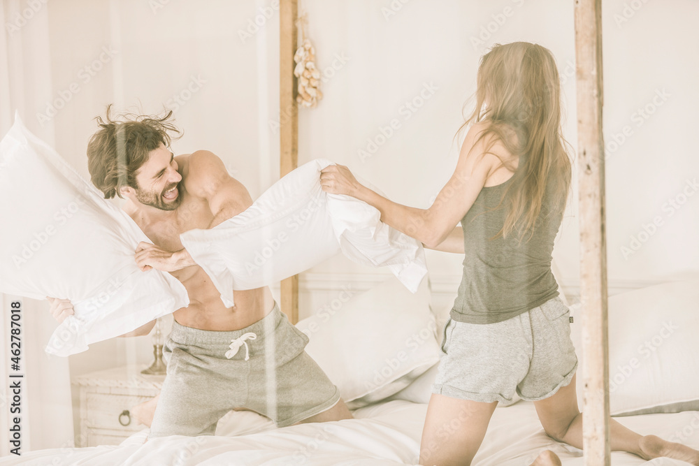 Carefree young couple having a pillow fight in bed Carefree young couple having a pillow fight in bed