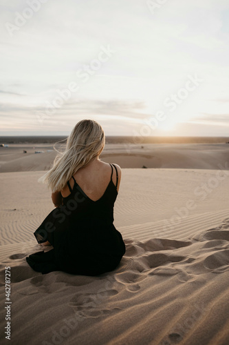 Back view of blond woman sitting on sand dune watching sunset, Algodones Dunes, Brawley, USA