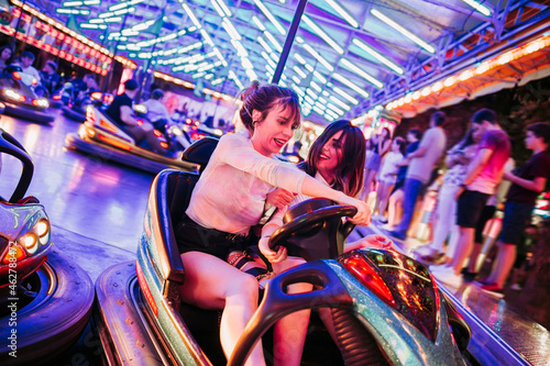 Two young women riding bumbper car on a funfair at night