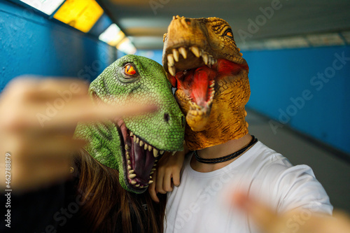 Male and female friends showing middle finger while wearing dinosaur mask in corridor photo
