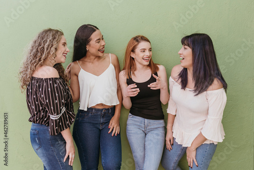 Multi ethnic female friends gossiping while standing against green wall photo