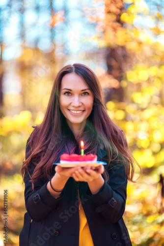 Beautiful woman with a birthday cake outdoors in the autumn forest