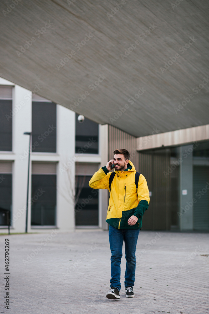 Smiling man on thephone walking along building in the city Smiling man on thephone walking along building in the city