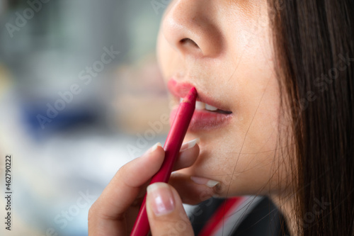 Beautiful asian woman applying red lipstick pencil on her lips