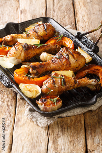 Grilled chicken legs with seasonal vegetables close-up in a grill pan on the table. vertical