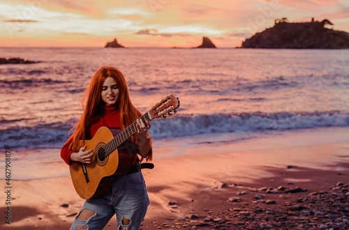 Portrait of redheaded young woman playing guitar on the beach at sunset, Almunecar, Spain photo