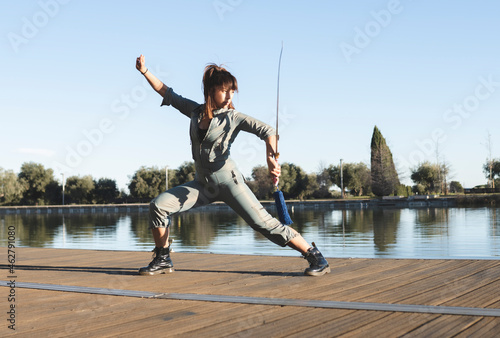 Confident female athlete with sword performing martial arts with dedication by lake on sunny day photo