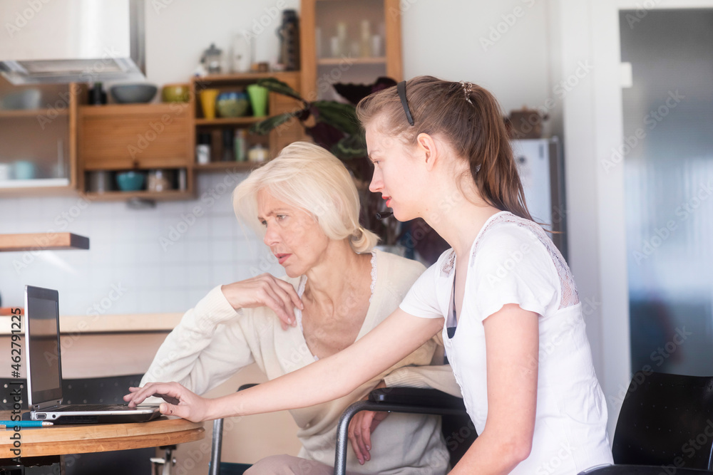 Daughter and mother in a wheelchair using a laptop Daughter and mother in a wheelchair using a laptop