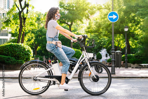 Woman riding electric bicycle on street during COVID-19 photo
