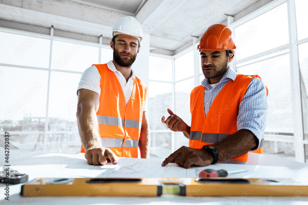 Two engineers man looking at project plan on the table in construction site Two engineers man looking at project plan on the table in construction site