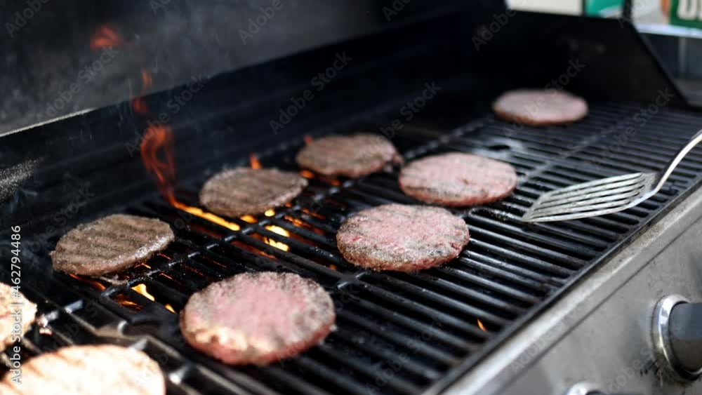 Male hand flipping raw hamburger meat on iron barbecue grill Male hand flipping raw hamburger meat on iron barbecue grill