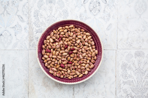 Bowl of dried pinto and borlotto beans lying on tiled surface photo