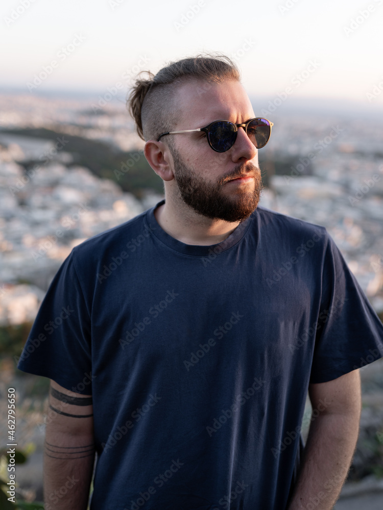 Portrait of young man posing with sunglasses, beard and ponytail during sunset Portrait of young man posing with sunglasses, beard and ponytail during sunset