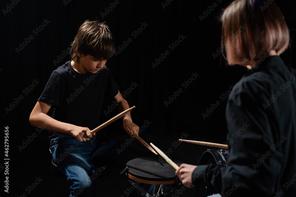 Young caucasian woman teaches a boy to play the drums in the studio on a black background. Music school student Young caucasian woman teaches a boy to play the drums in the studio on a black background. Music school student