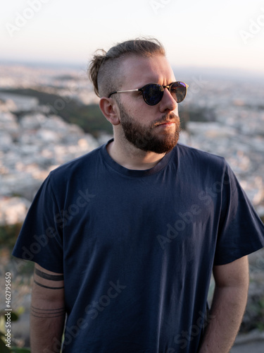 Portrait of young man posing with sunglasses, beard and ponytail during sunset