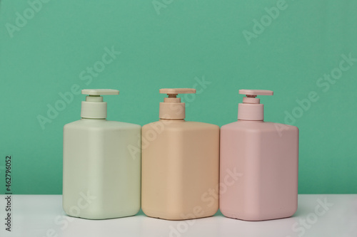 Three bottles for cosmetics with dispensers of different colors for soap, shower gel, shampoo, hair conditioner, on a green background