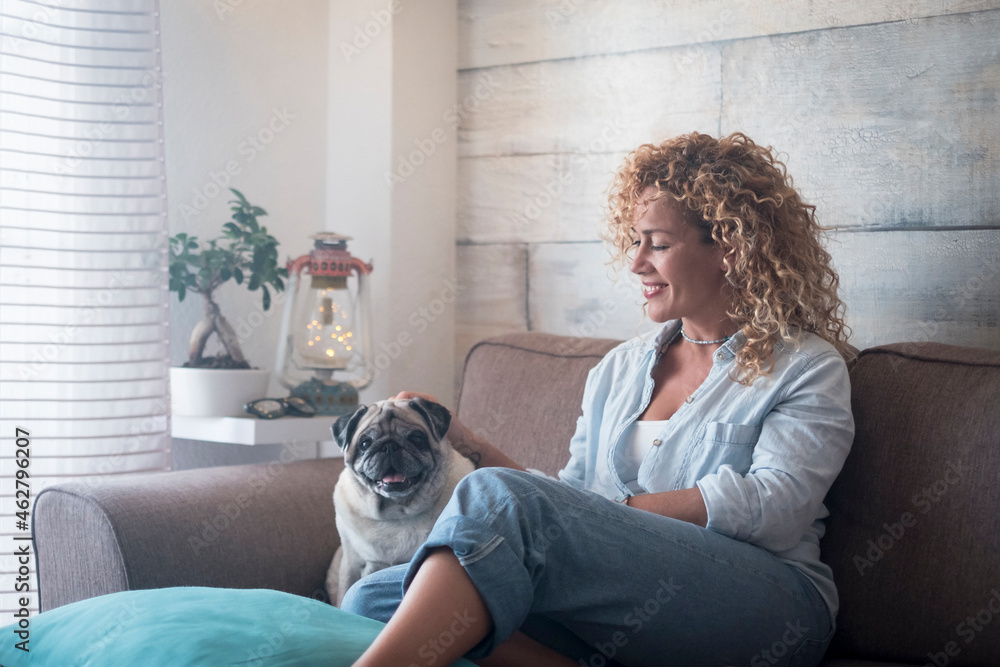Woman sitting on couch at home petting pug dog Woman sitting on couch at home petting pug dog