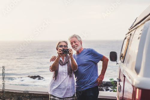 Senior couple traveling in a vintage van, taking pictures at the sea photo