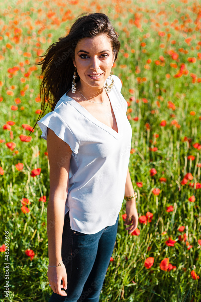 Smiling beautiful woman standing at poppy field during springtime