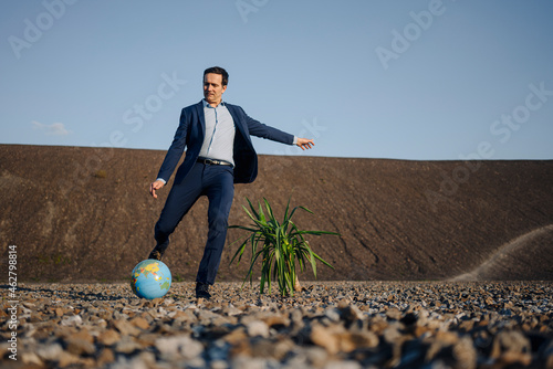 Mature businessman playing soccer with a globe on a disused mine tip photo