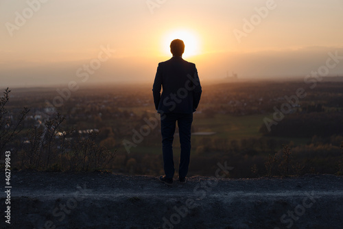 Mature businessman standing on a disused mine tip at sunset looking at view photo